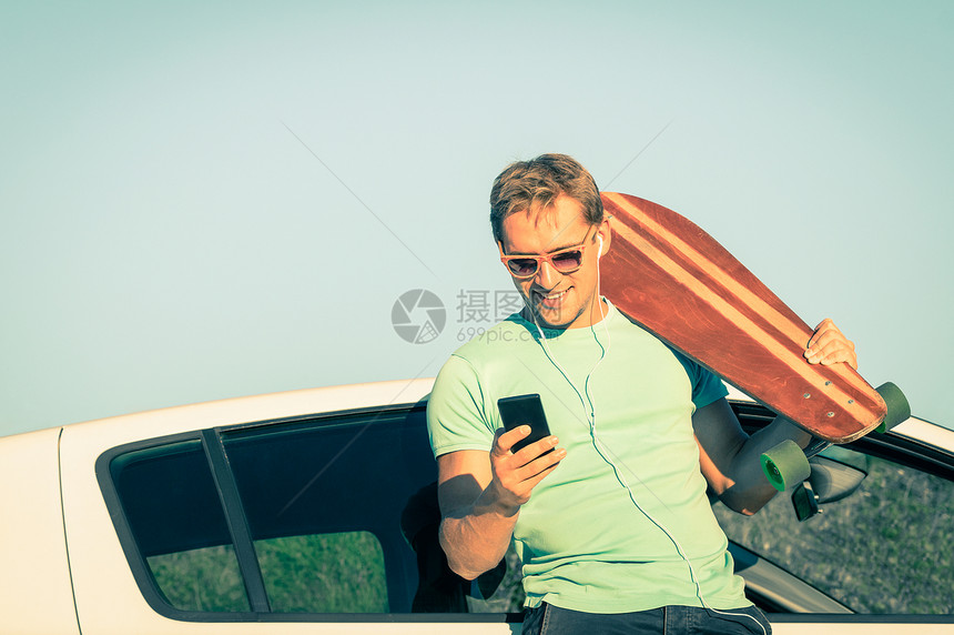 年轻的潮人在旅途中在他的车旁休息时用智能手机听音乐新趋势和现代技术的概念与复古的生活方式相结合柔和的不饱和图片