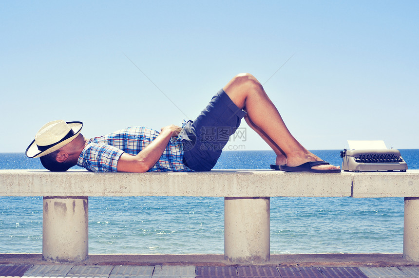 一台空白页的旧打字机和一个年轻人躺在海边的街头长椅图片