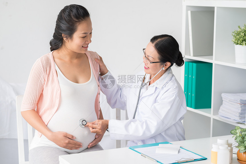 听孕妇肚子的有听诊器的亚洲医生图片