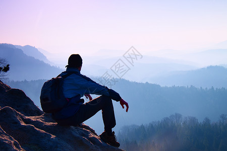 背着运动背包的游客坐在岩石山峰上图片