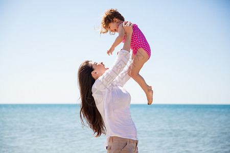 一个年轻母亲在海滩上玩得开心并在空中抬起她女儿的景象图片