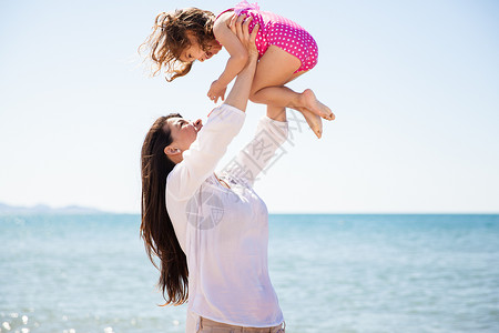 年轻母亲在海滩玩得开心时将女儿抬起图片