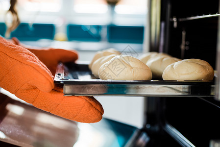 烤箱中面包在金属饼干板旁边用持锅手举着图片
