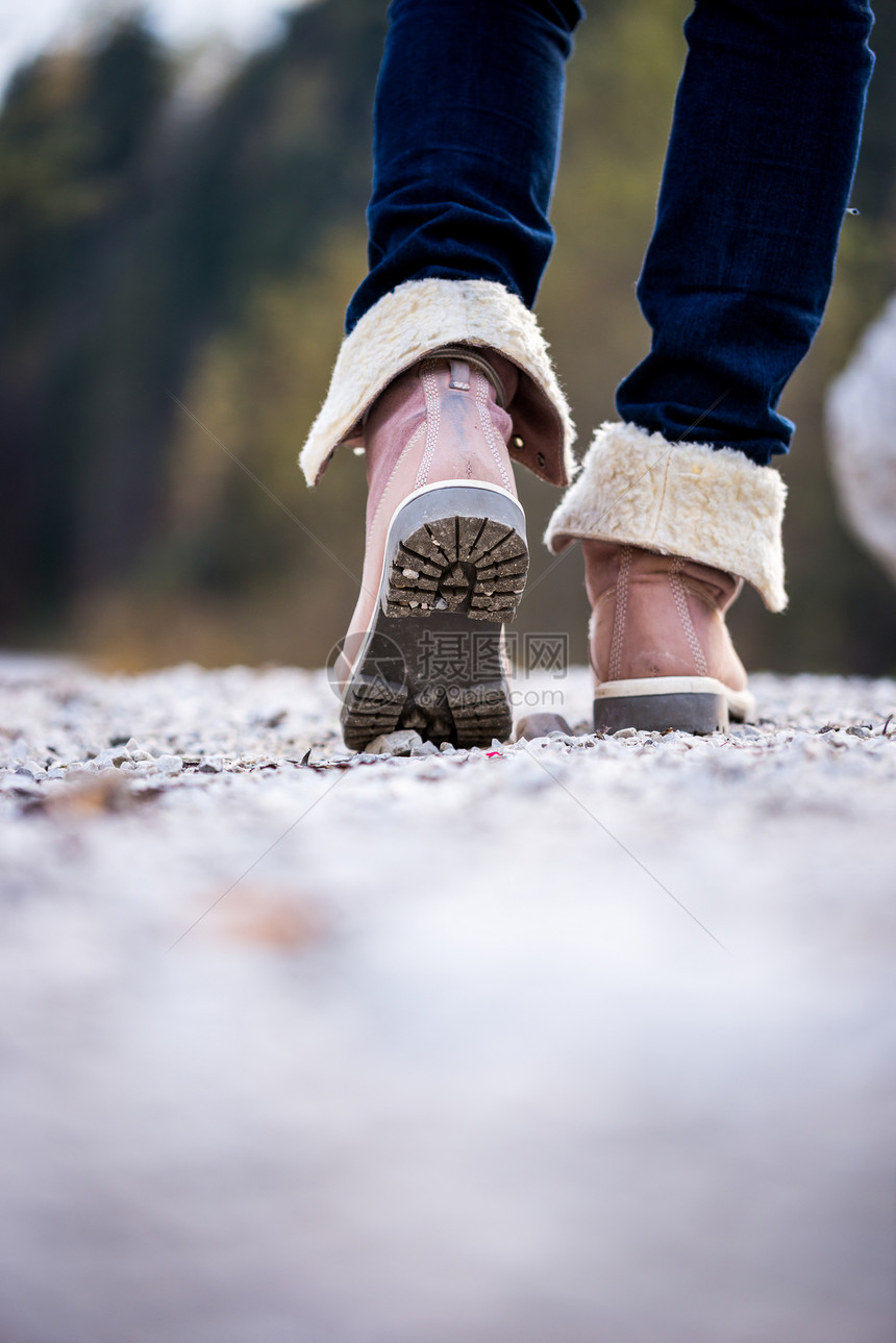 一个穿着牛仔裤和脚踝高的皮靴沿着远离相机的乡村小路行走的女人的脚低角度视图户图片