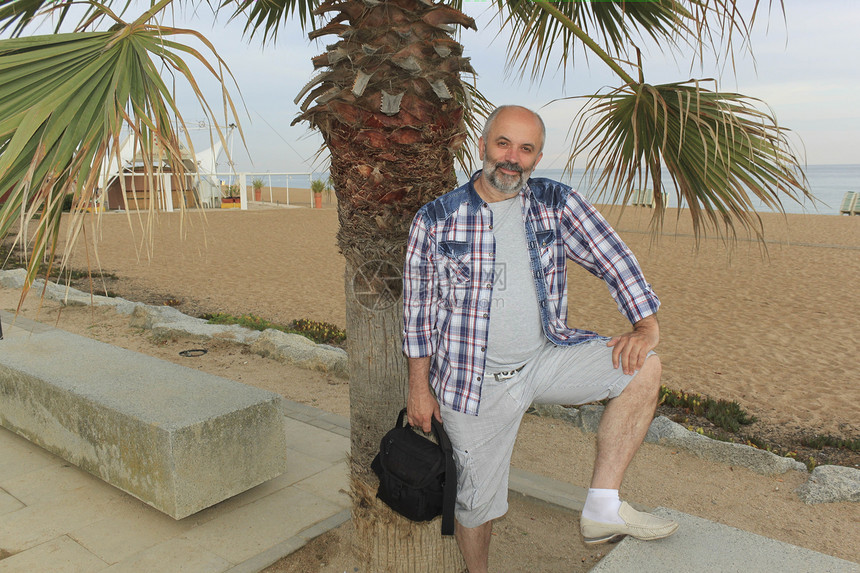 以棕榈树沙滩和大海为背景的中年男子图片