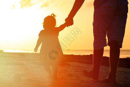 走在沙滩上的父亲和小女儿的剪影图片