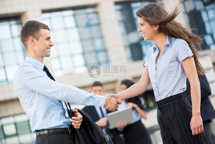年轻的女商人和商人在公司面前握手图片