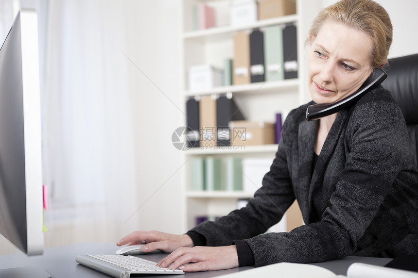 女商人在她的书桌里和电脑打字时的电图片