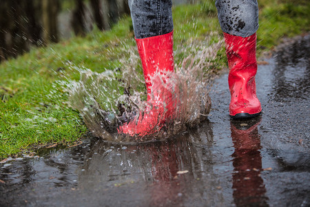 身穿红雨靴的女子跳进水坑里图片