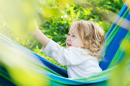 两岁幼童女孩在夏季花园的巴西蓝绿色吊床上大笑和玩耍图片