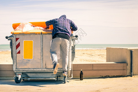 年轻的流浪汉在垃圾箱里翻找食物和可重复使用的商品图片