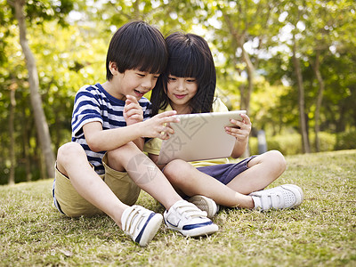 小亚洲女孩和男孩坐在草地上图片