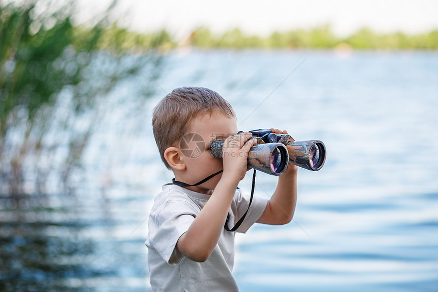 小男孩在河岸上透过望远图片