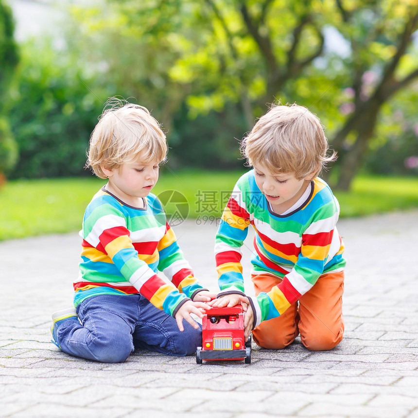 两个穿着五颜六色衣服的小朋友在温暖的阳光明媚的日子里在夏日花园里玩红色木制巴士玩具一起学图片