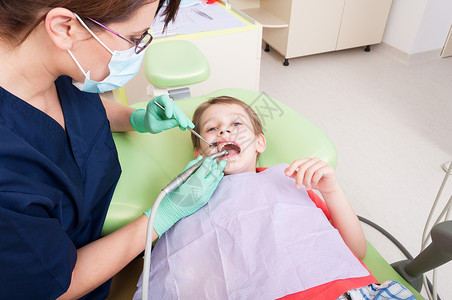 害怕在牙医椅上进行钻孔手术的孩子与儿童患者一起工作的女或图片