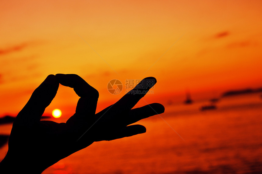 一个年轻人在日落时用手打坐禅宗手印的特写镜头图片