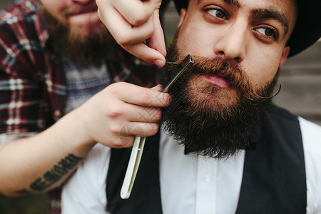 理发师在复古的氛围中给留胡子的人刮胡子图片