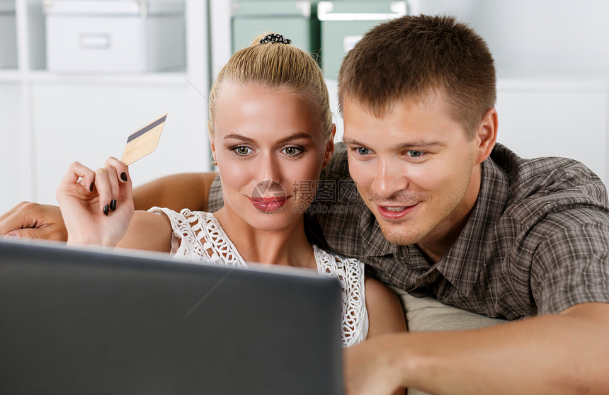 家庭夫妇通过互联网在笔记本上购物并用信卡付款丈夫和妻子在家里买新东西购物消费主义交图片