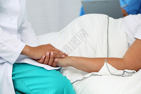 友好的女医生手牵着孕妇的手躺在床上图片
