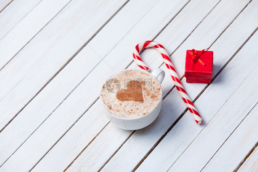 一杯有心脏形状的咖啡和圣诞糖果在白色木头背景的图片
