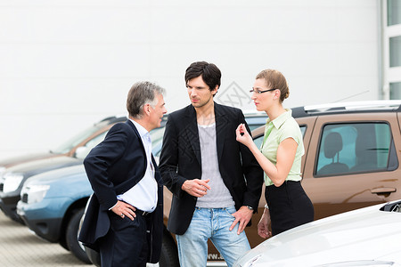 站在车中间的停车场上的成熟男人和年轻夫妇图片