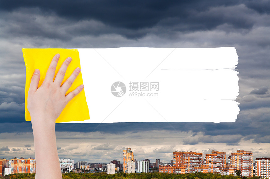 手从图象上用黄色抹布删除城市住宅上空的雨云图片