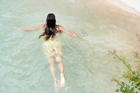 一个迷人的年轻女子在温泉天然游泳池清澈的海水中游泳的头顶后方美景图片