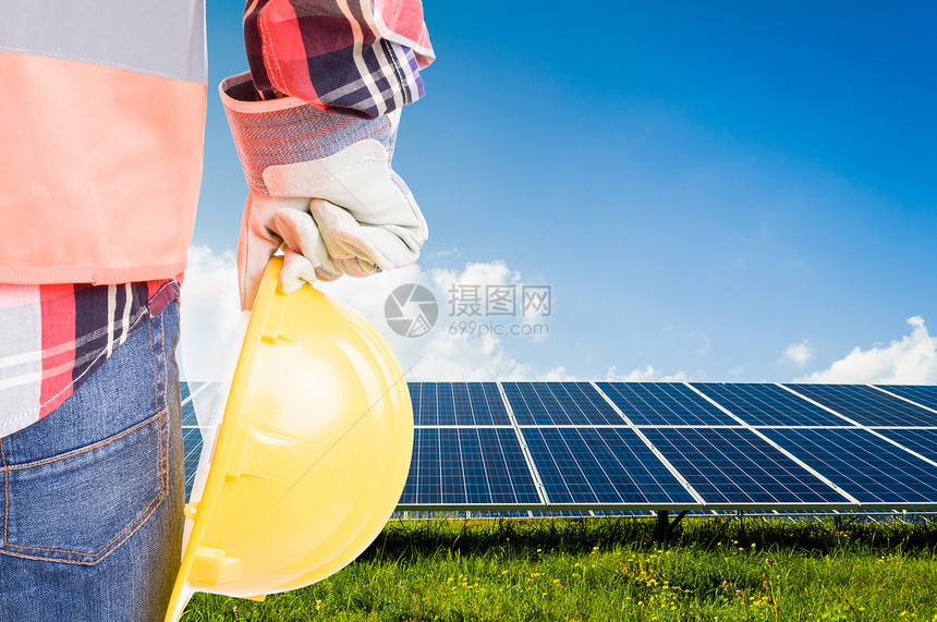 工程师在太阳能光伏板背景上持有安全帽构建未来可再生能源解决图片