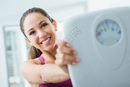 快乐的年轻妇女减体重和显示一个规模饮食和健身概图片