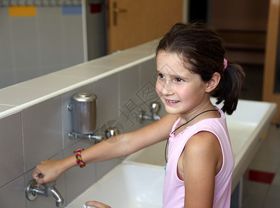 小女孩在洗手在学校浴室的水槽背景图片