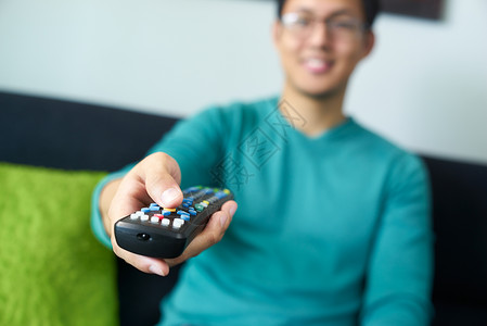 以遥控方式观看电视和换频道的亚洲青年成男子近距离关注按钮和手图片