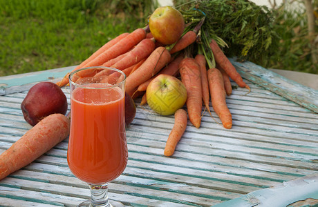 一杯新鲜的苹果胡萝卜汁在木质表面上背景中的新鲜胡萝卜和苹图片