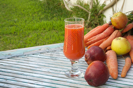 一杯新鲜的苹果胡萝卜汁在木质表面上背景中的新鲜胡萝卜和苹图片