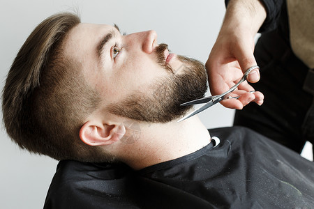理发师剪刀的年轻英俊客户的胡子用白色背图片