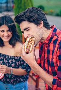 年轻人吃着美国热狗女人笑着背景在户外的夏日烧烤中与朋背景图片