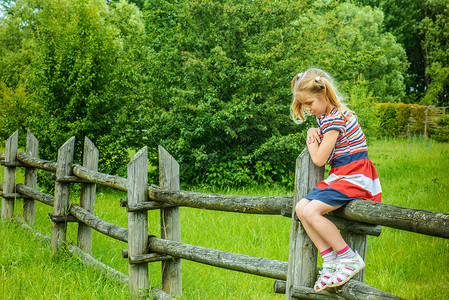 坐在农村木篱上的美丽的悲伤小女孩图片