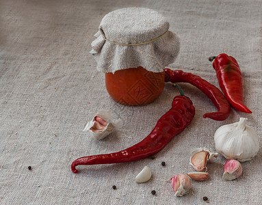 在油布上热辣椒和大蒜旁边的玻璃罐子里自制的土制图片