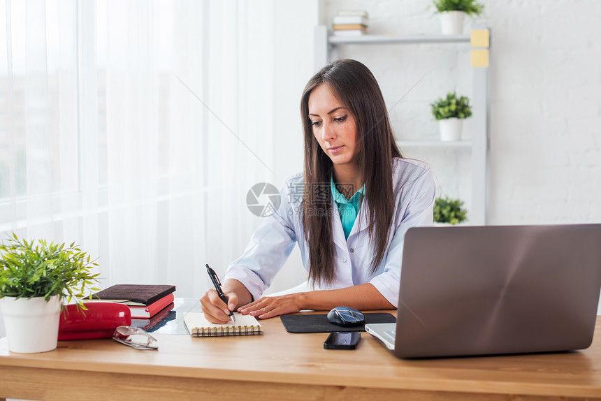 在医疗办公室工作场所工作的医生在书桌旁写处方的肖像图片