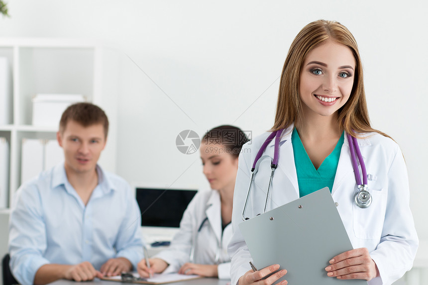 微笑的女医学生与她的同事在背景中咨询男患者的肖像医疗保图片