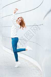 穿着白色毛衣蓝色牛仔裤和穿白鞋跳跃的漂亮女孩图片