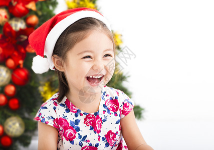 快乐的小女孩圣诞树前戴着圣诞红帽子图片