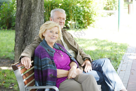 坐在公园和放松时对着镜头微笑的情侣图片