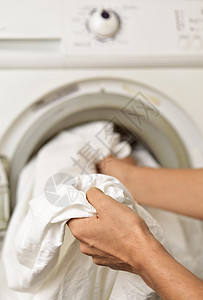 一个年轻人将白床单引入或取出洗衣机或图片