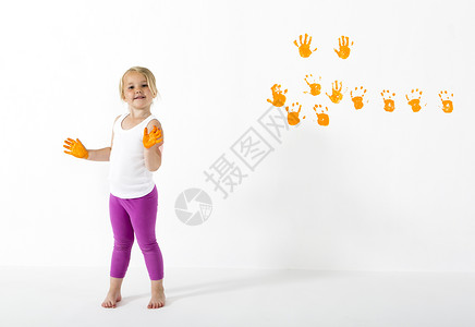 用橙色和手印画白墙的小女孩图片