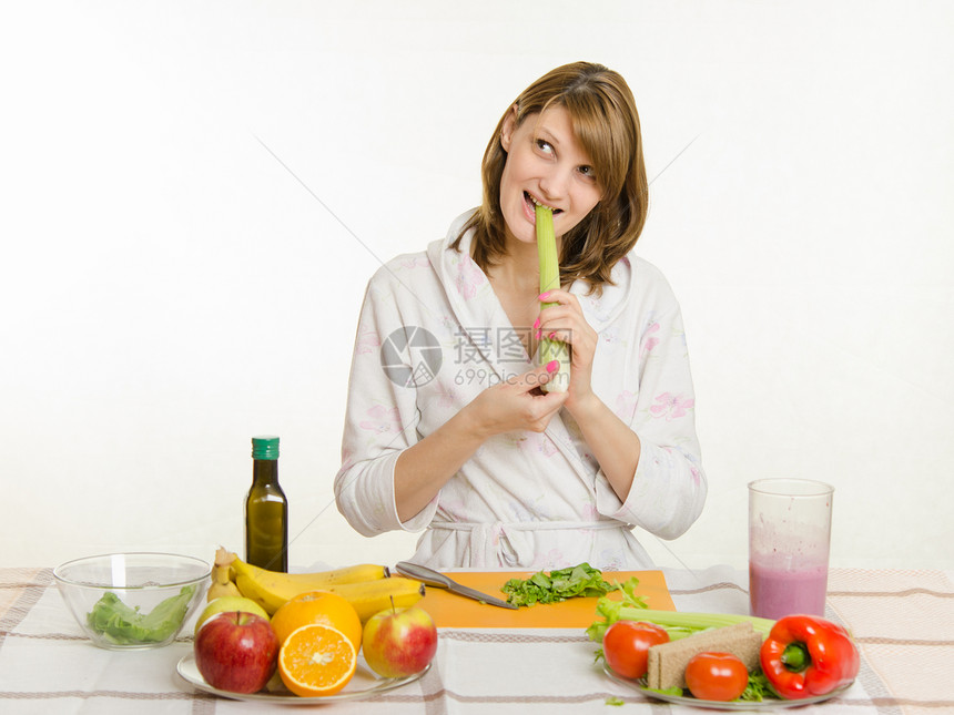 穿浴袍的年轻美女准备素食沙拉从蔬菜和绿菜中提取白种背图片