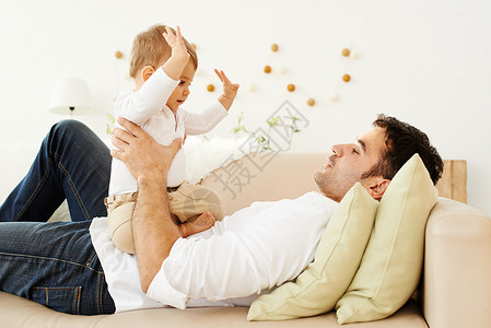 父亲躺在沙发上和他的小儿子玩耍图片
