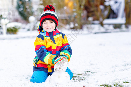 穿着多彩衣服的漂亮男孩做雪人图片