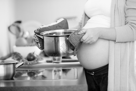 将金属锅放在厨房里的孕妇的黑图片