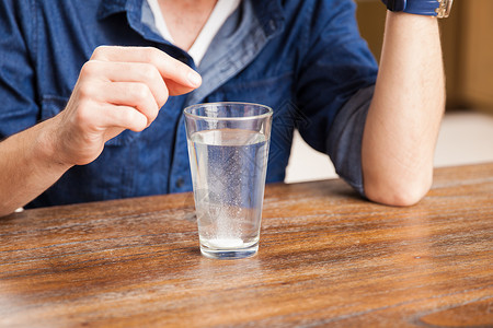 一名年轻人在杯水中倒着晚月药片的一对年背景图片