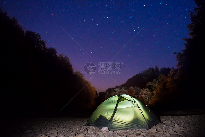 夜间在深蓝天空下林中与许多星共聚一气的图片